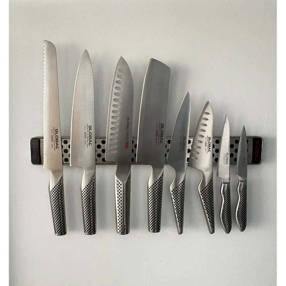 Set of eight stainless steel Global kitchen knives on magnetic knife rack mounted on white wall