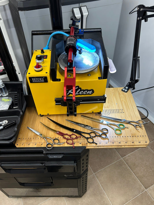 Professional scissor sharpening machine with multiple pairs of hairdressing scissors laid out, used by Sharpening Services Somerset for in-salon sharpening services.