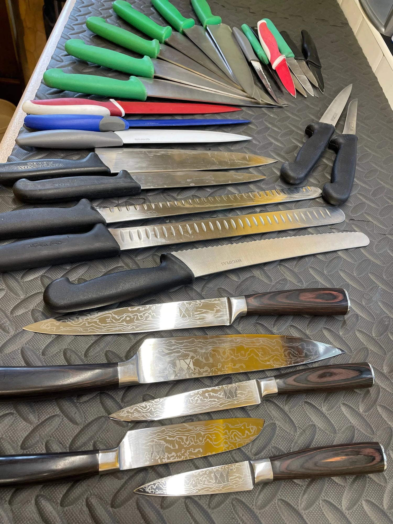 Various sharp knives with colorful, black, and wooden handles neatly arranged on a textured black surface