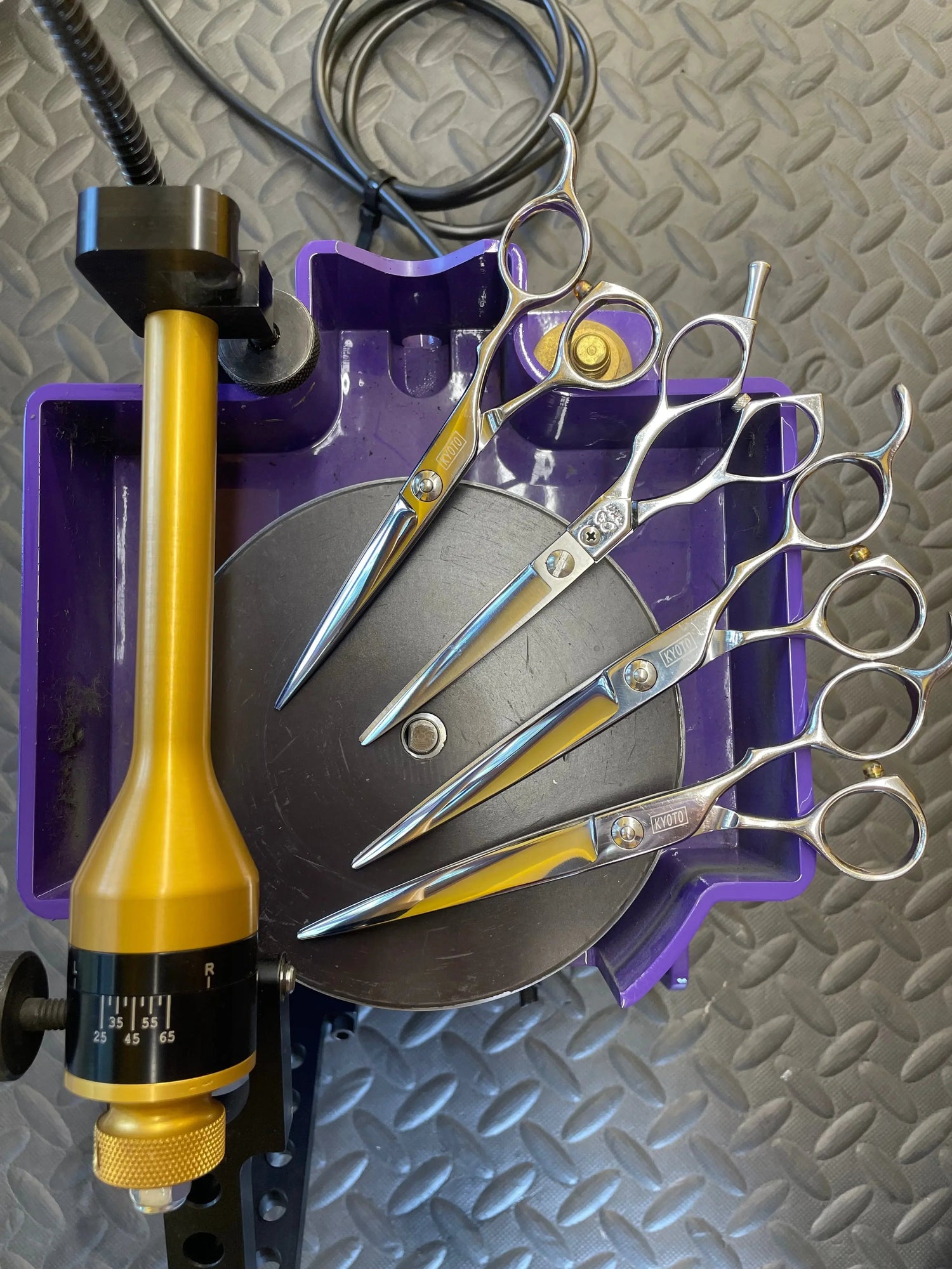 Four shiny Kyoto hair cutting shears on a purple sharpening tool with a gold and black adjustment dial