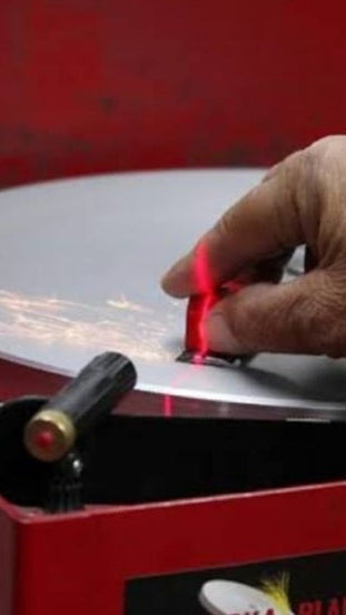 Hand Holding a clipper blade on a machine called the big red. it has a laser light and sparks coming from it