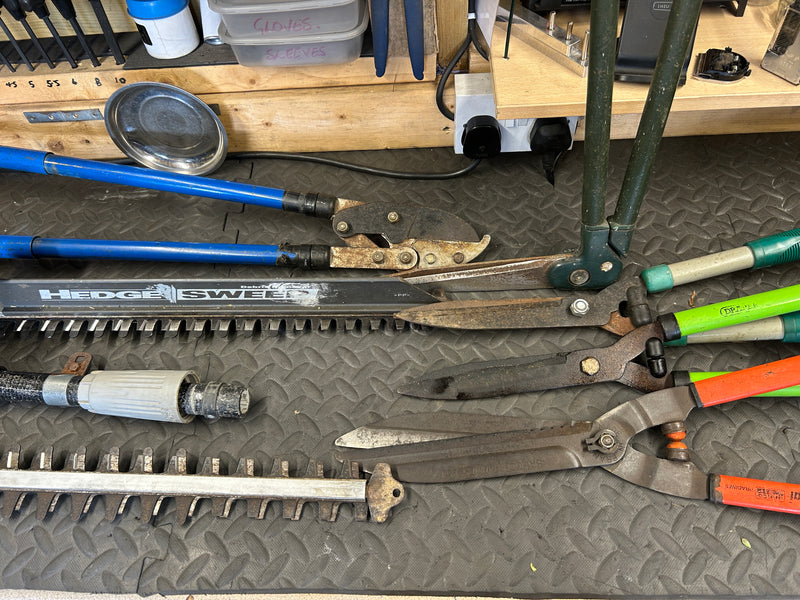 Collection of garden tools including shears and hedge trimmers on a workbench.