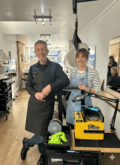 Two people in a salon setting with a yellow appliance and aprons.