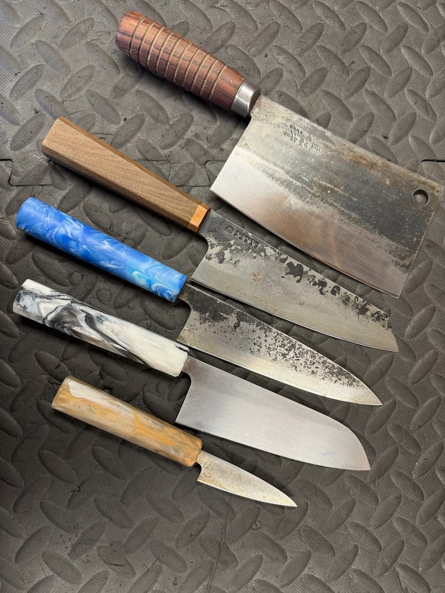 Six kitchen knives with mixed handle styles laid out on a textured mat, ideal for professional knife sharpening services.