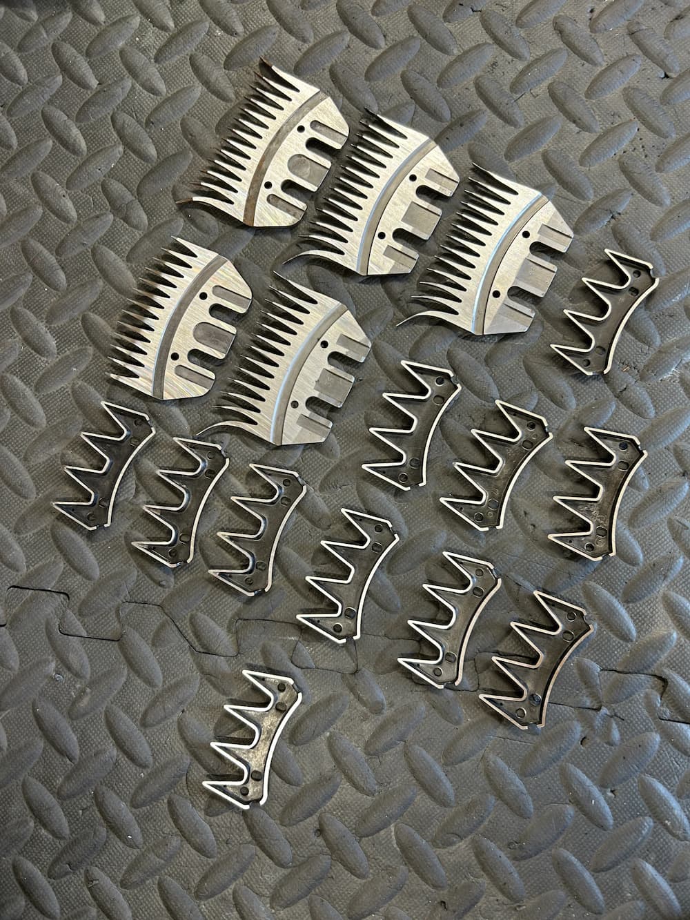 Clipper blades and comb attachments arranged on a textured mat, ideal for professional clipper blade sharpening services.