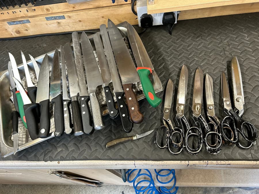 Assorted kitchen knives and tailor’s shears laid out on a workbench, ready for professional sharpening services.