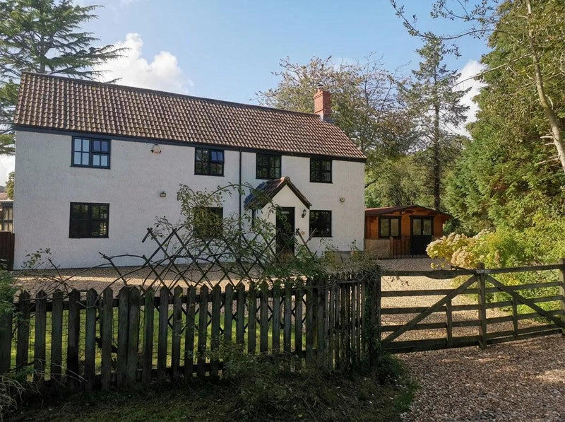 White house with brown roof in a rural setting with trees and a wooden gate.