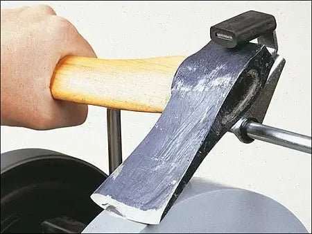 Small axe being sharpened on a Tormek wet grinding wheel with a wooden handle held by a hand