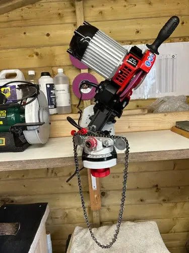 Electric chainsaw sharpener mounted on a workbench in a wooden workshop with tools and bottles nearby
